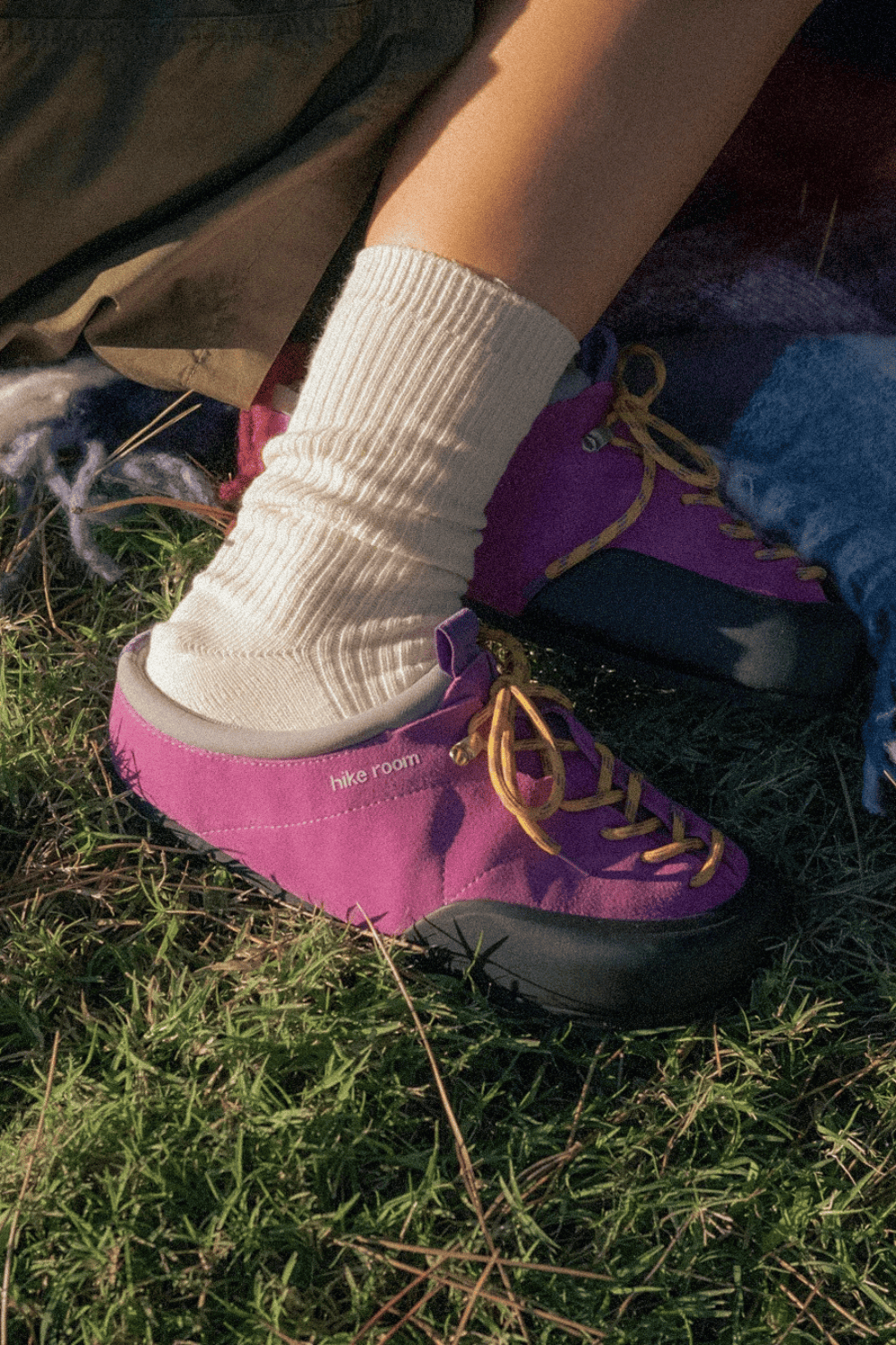 primer plano de un pie sobre la hierba calzando un zueco morado de la marca Hike Room, con puntera de goma negra y cordones amarillos de escalada.
