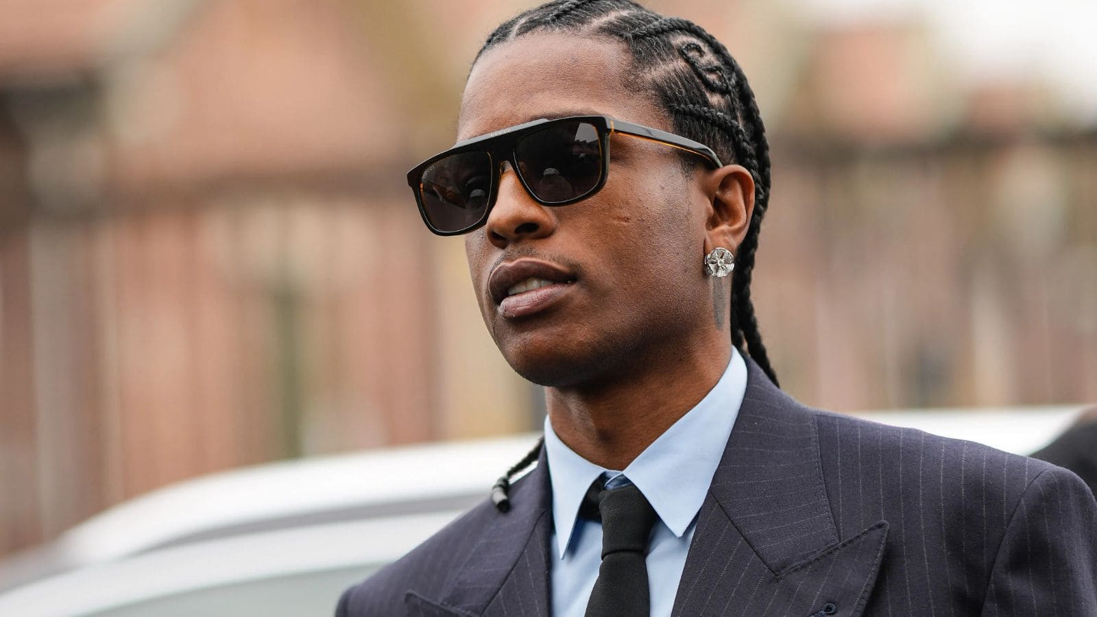 A$AP Rocky con traje de raya diplomática, camisa azul y corbata negra, ejemplo de look formal elegante para una cita