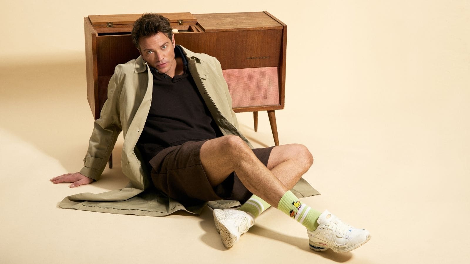 Modelo masculino con gabardina, zapatillas deportivas blancas y calcetines verdes de la colección Barrio Sésamo de BESOCKS